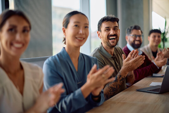 Happy colleagues applauding after successful business meeting in office.