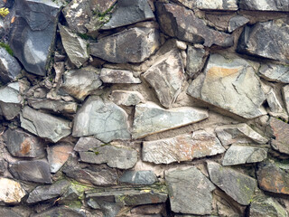 Texture of an old stone wall made of rough rocks with moss and cracks. Natural stone background.