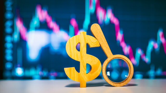 Magnifying glass with dollar icon. backed by a stock monitor screen, representing investor strategies and both short- and long-term stock market investments.