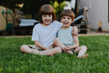 Fototapeta premium Happy children sitting on green grass, enjoying a sunny day while smiling and playing together in a cheerful outdoor setting, capturing moments of childhood joy.