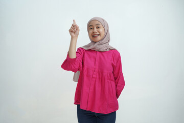 Smiling Young Asian Muslim Woman in Hijab Pointing with Both Hands on isolated background