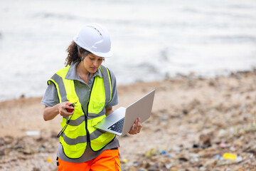 Environmental Scientist Conducting Beach Cleanup Survey, Female Engineer Using Laptop for Coastal Area Assessment, Worker in Safety Vest and Hard Hat Documenting Outdoor Site
