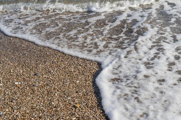 Close-up of gentle sea wave rolling on sandy shore. Sparkling sea water and foam on shore at sunset
