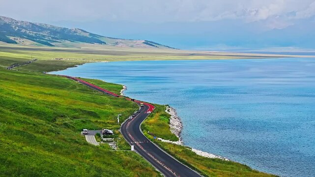 Aerial shot of winding road and blue lake with green grasslands in Xinjiang. Beautiful Sayram Lake natural landscape in China.