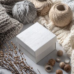 White box surrounded by yarn, knitted fabrics, and dried plants