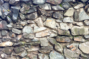 Texture of an old stone wall made of rough rocks with moss and cracks. Natural stone background.