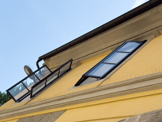 Open windows on slanted roof of yellow building under blue sky