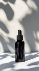 A black glass dropper bottle sits on a white surface. Soft shadows create an artistic pattern on the background, emphasizing the bottle's sleek design.