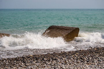 A large rock is in the ocean, and the water is crashing against it