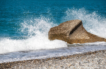 A large rock is in the ocean, and the water is crashing against it