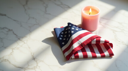 Folded american flag rests beside a softly glowing candle on a marble surface, bathed in gentle sunlight