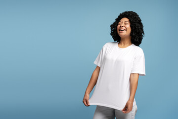 African American woman with closed eyes laughing in oversized white t-shirt on blue background
