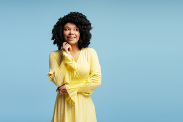 Happy young African American woman in bright yellow dress on blue background