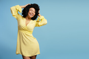 Happy pretty African American woman in yellow dress posing in studio, closing eyes