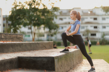 Fototapeta premium A young woman takes a break after exercising, relaxing with a cheerful smile. She wears headphones, listens to music, and chats with her friend on the phone, enjoying the peaceful moment.
