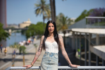 Young woman, brunette, tall, slim and very tattooed, wearing white top and denim skirt, posing...