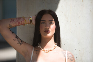 Portrait of young woman, brunette, tall, thin and very tattooed, with white top, posing looking at...