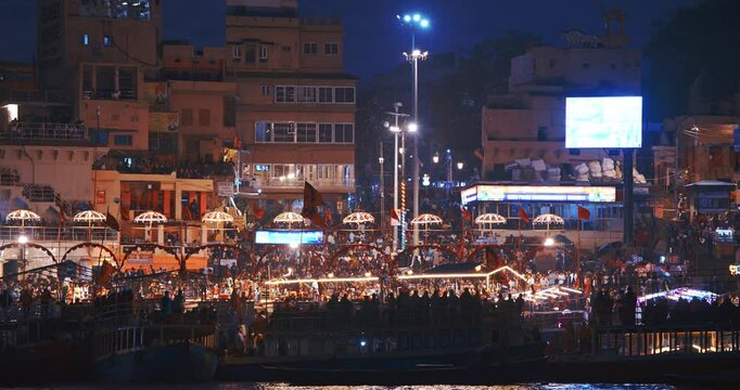 Varanasi, Uttar Pradesh, India. Many people visiting Ganga Maha Aarti ceremony on Dashashwamedh Ghat. night time illumination lights. Cinematic Camera movement moving along riverbank embankment. View