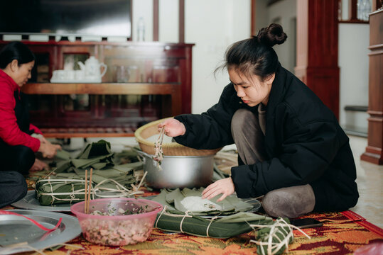 Young Asian women prepare traditional food using leaves in a cozy home setting during the daytime in Vietnam