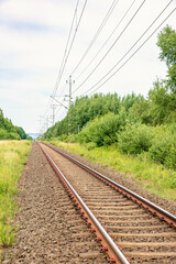 Railway with electric wires through a green deciduous forest in summer