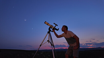 Amateur astronomer using telescope for watching stars, Moon, planets and other celestial objects from a countryside field in nature.