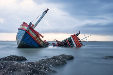 Old wrecked fishing boat in sea at dusk on coast of Ang Sila Village, Saensuk Sub-district, Chonburi Province of thai Suite for storm, natural disaster, surge, severe weather, loss and disappointment.