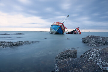 Old wrecked fishing boat in sea at dusk on coast of Ang Sila Village, Saensuk Sub-district, Chonburi Province of thailand. Suite for feelings of loss, disappointment, loneliness, emptiness and storm.