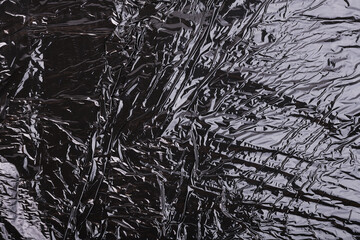 Textured black crumpled plastic film that reflects light artistically.