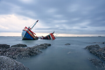 Old wrecked fishing boat in sea at dusk on coast of Ang Sila Village, Saensuk Sub-district, Chonburi Province of thailand. Suite for feelings of loss, disappointment, loneliness, emptiness and storm.