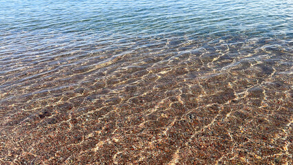 Clear lake water and pebble bottom under sun reflections