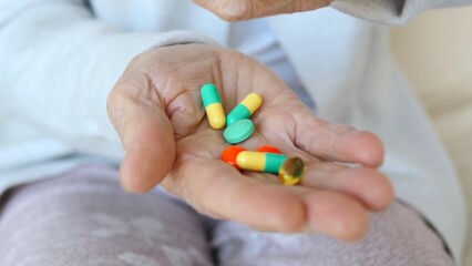 Close up of wrinkled hand holding variety of pills, highlighting challenges of medication...