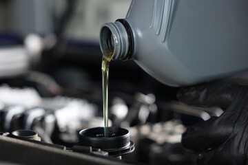 Pouring motor oil from bottle into car engine, closeup