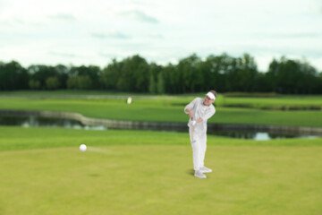 Golfer hitting ball with club on course, selective focus
