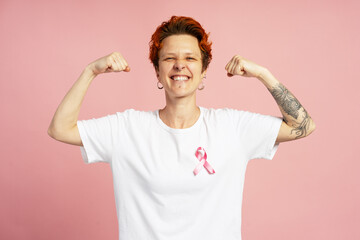 Strong woman with pink ribbon showing biceps and smiling