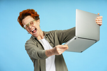 Excited businesswoman shaking laptop and screaming on blue background