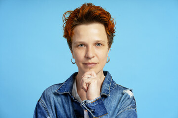 Confident young woman with orange hair and piercings posing on blue background