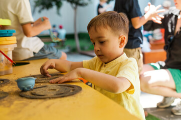 Boy playing with sand and pretend outdoor kitchen during summer daycare playtime. Imaginative and sensory activity for toddlers