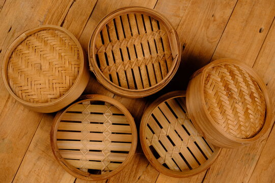 a collection of bamboo steamers and food containers made of woven bamboo on rustic brown wood. Indonesian traditional cooking ware. kukusan bambu. klakat bambu. Chinese bamboo cooking ware. dim sum. 