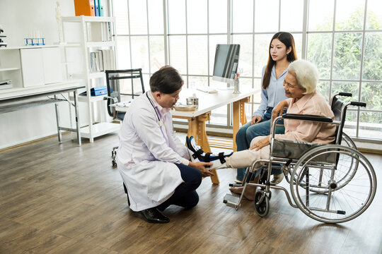 A senior woman in a wheelchair receives orthopedic care from a doctor while a caregiver looks on. The image highlights mobility support, elder rehabilitation, and compassionate medical attention. - Powered by Adobe