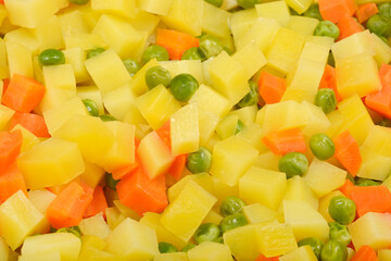A vibrant close-up shot captures a mix of cooked, diced potatoes and carrots along with green peas, perfect for a fresh salad