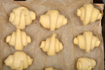 An overhead close-up of raw, rolled croissant dough pieces arranged on parchment paper before baking