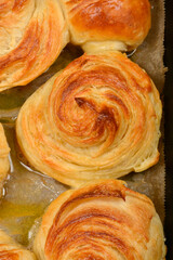 A top-down close-up captures the spiraled, golden-brown tops of freshly baked croissants, glistening with butter on parchment paper