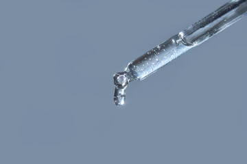 Close-up of transparent liquid drop from glass pipette against light blue background.