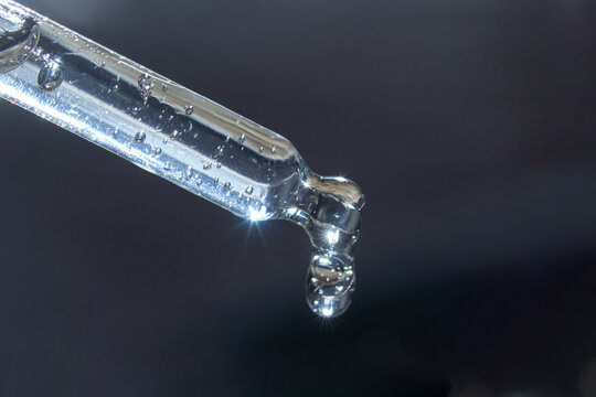 Close-up of transparent glass dropper with droplet against dark background.