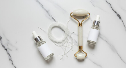 Collagen Threads Next to Face Roller and Serum Bottles Flat Lay on Marble