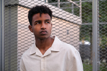 Portrait of a stylish young man standing near a metal fence in an urban setting, looking away from...