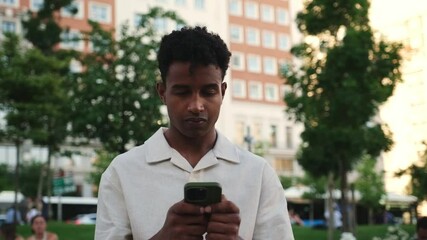 Portrait of a young man using his smartphone and smiling in a city park