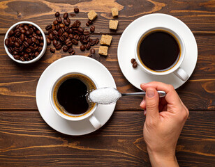 black coffee in a glass, hand adding sugar with a spoon, seen from above, on a dark wooden background