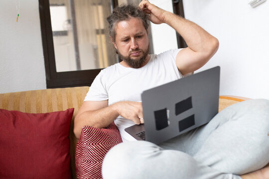 Confused freelancer scratching head while working on laptop at home