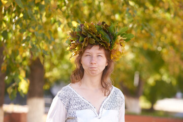 Young caucasian female with leaf crown expressing joy amidst autumn trees.